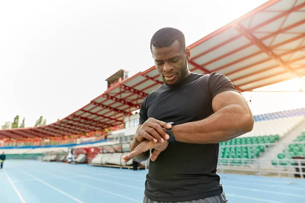 Handsome strong man standing and looking at smartwatch during training. — Stock Photo, Image