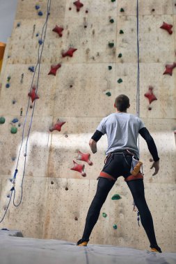 Ön kolsuz güçlü kaya tırmanıcısı, yüksek yapay tırmanma duvarının önünde duruyor