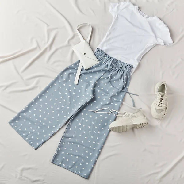 Голубые брюки с червями, белая футболка, кроссовки и сумка, лежащая на кровати — стоковое фото