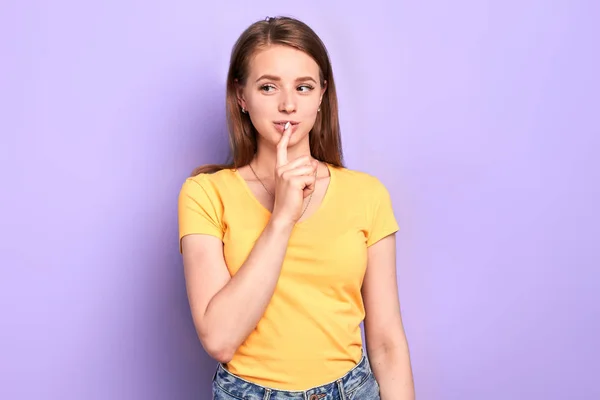 Vrouwelijke student staat zorgvuldig, houdt wijsvinger in de buurt van lippen — Stockfoto