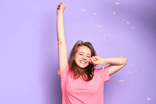 Happy girl dancing under flying feathers with closed eyes during pillow fight party — Stock Photo, Image