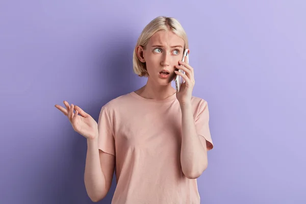 Chateado, triste, cético mulher falando no celular isolado violeta fundo — Fotografia de Stock