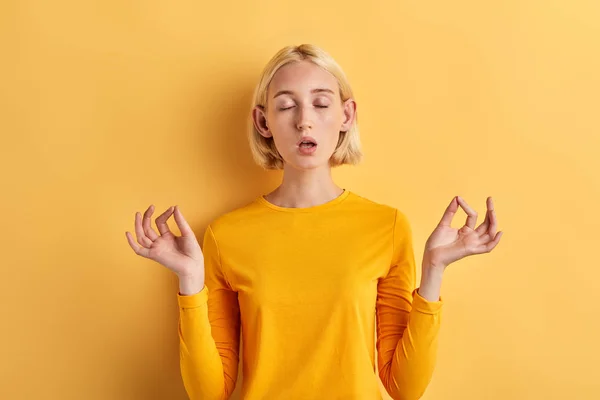 Расслабленная молодая женщина медитирует с закрытыми глазами на желтом фоне — стоковое фото