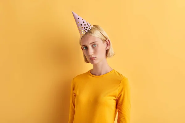 Una joven deprimida infeliz en un sombrero de cumpleaños esperando a los invitados —  Fotos de Stock