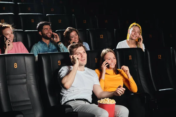 Grappige jonge mensen die telefonisch praten en lachen terwijl ze in de bioscoop zitten — Stockfoto