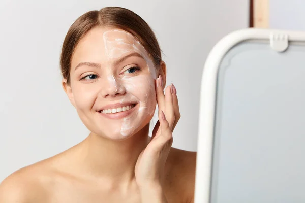 Jovem menina positiva aplicando creme no rosto — Fotografia de Stock