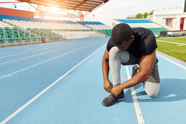 Sportsman ties his trainers, sitting on the running track, preparing — Stock Photo, Image