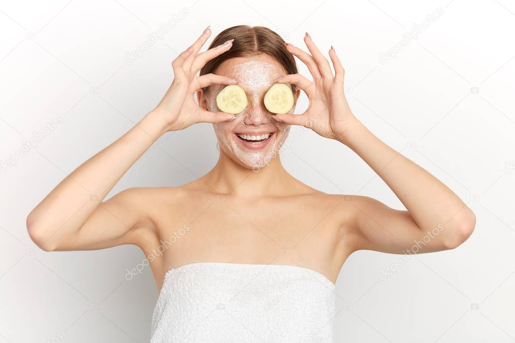 smiling girl with facial mask and cucumber slices in her hands having fun