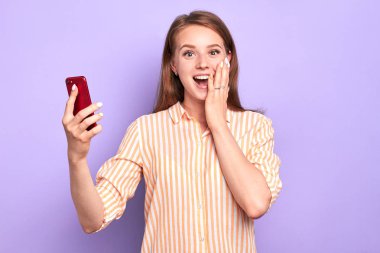 Suprised funny young woman smiling broadly, holding red cell phone clipart