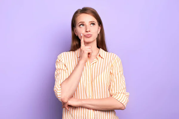 Dreamy pretty female keeps index finger near lips, looking somewhere above — Stock Photo, Image