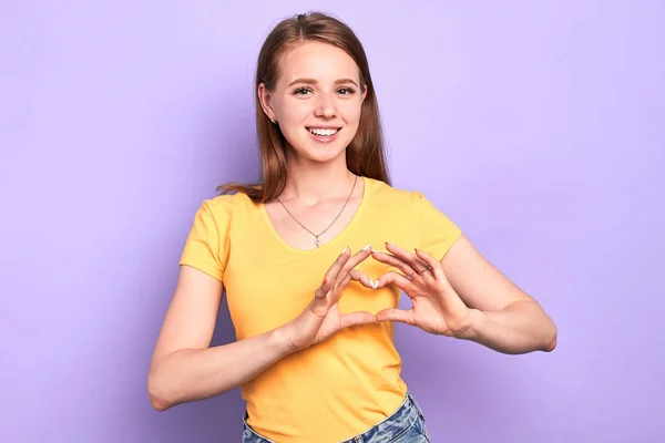 Adorable happy female teenager makes heart gesture with hands over chest
