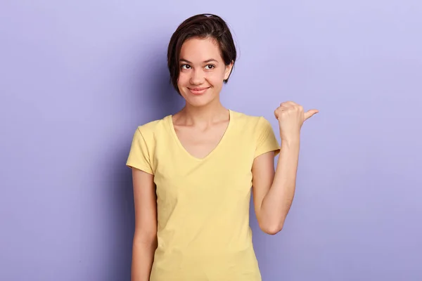Lächelnde brünette Frau in stylischem gelben T-Shirt, die wegschaut und wegzeigt — Stockfoto