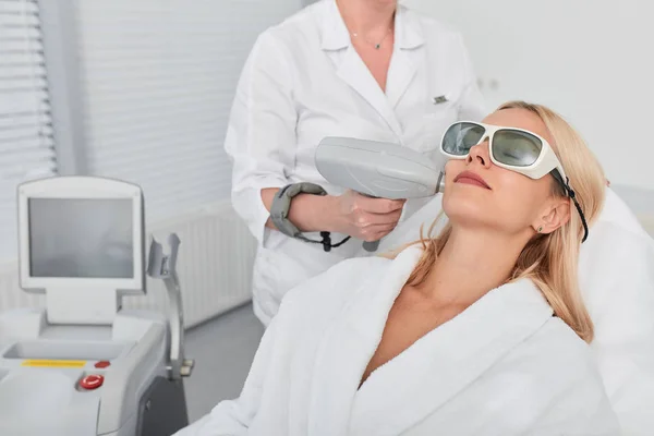 Cliente feminino vestindo óculos e roupão de banho branco descansando na clínica de beleza — Fotografia de Stock