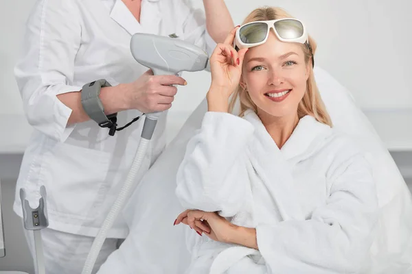 Donna allegra con gli occhiali sulla fronte che si prepara per le procedure di pelle laser — Foto Stock