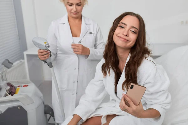 Rolig brunett kvinna i vit badrock sitter på skönhetssalongen och tar en selfie — Stockfoto