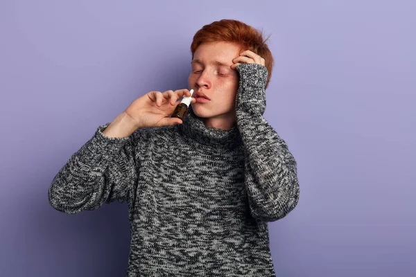 Sick young poor man in stylish gray sweater taking nose drops — Stock Photo, Image