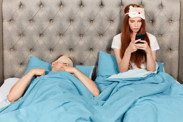 Красива дівчина-імбир читає своїм чоловікам балачки, поки він спить на ліжку — стокове фото