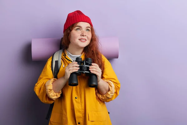 Aufgeregter Tourist mit Pflegematte, Rucksack, gelbem Mantel, Strickmütze, die nach oben schaut — Stockfoto