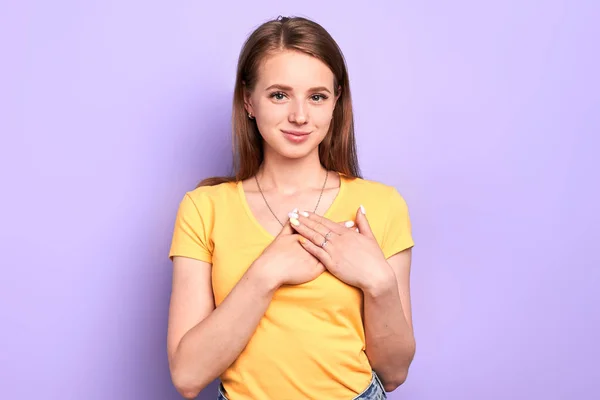 Schattige vrouw houdt beide palmen op het hart, kijkt in de camera met vriendelijke glimlach — Stockfoto