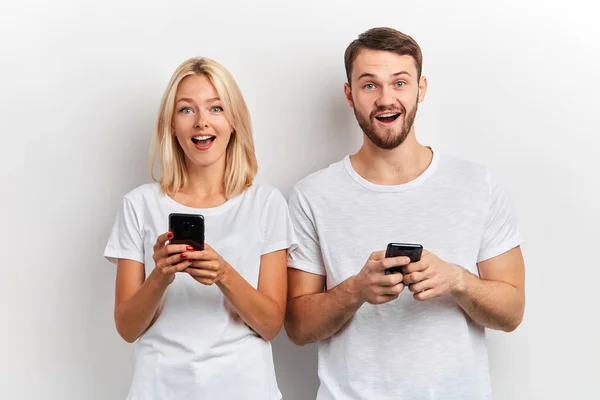 Emocionado feliz hombre y mujer con los teléfonos mirando a la cámara — Foto de Stock