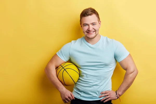 Guapo joven bien construido sosteniendo una pelota de baloncesto sobre un fondo amarillo — Foto de Stock