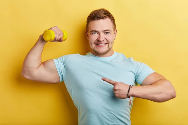 Positivo motivado deportista ambicioso apuntando a su brazo con mancuerna — Foto de Stock