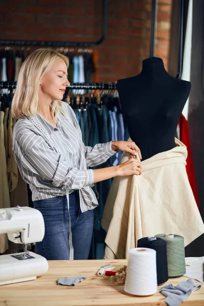 Blonde femalen designer measuring fabric on black dummy at work — Stock Photo, Image