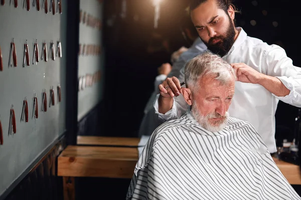young stylist trimming senior mans hair