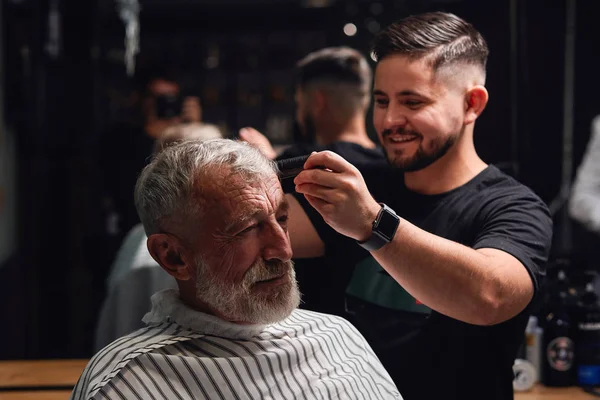 smiling awesome young barber brushing the hair of senior man