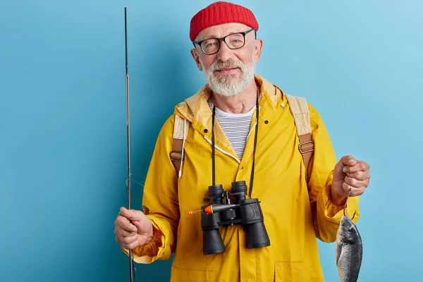 Доброзичливий красивий бородатий чоловік у стильному повсякденному одязі, що тримає рибу та стрижень — стокове фото
