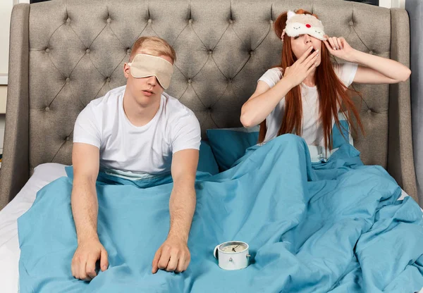 Jeune couple mignon en masques pour les yeux se réveillant le matin avec des difficultés . — Photo