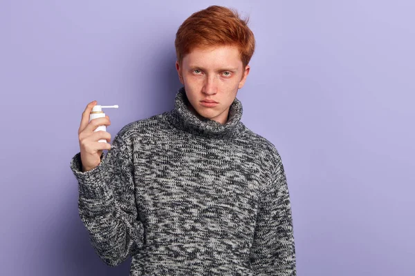 A sick poor man holding a nasal spray in his hand on blue background — Stock Photo, Image