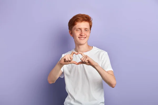 Retrato de un joven sonriente haciendo un gesto de corazón sobre un fondo azul —  Fotos de Stock