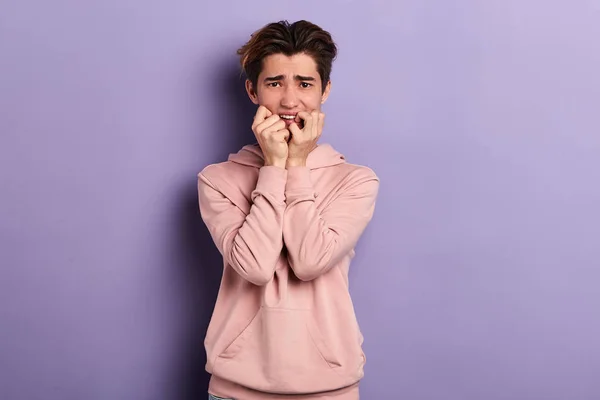 Emotional scared young man with hands under his chin on blue background — Stock Photo, Image