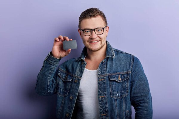 Happy positive attractive man wearing denim jacket showing credit card