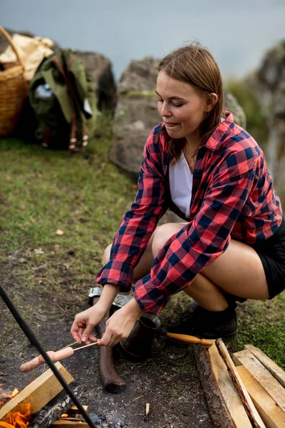 Bella ragazza concentrata su sedersi vicino al falò arrosto salsiccia — Foto Stock
