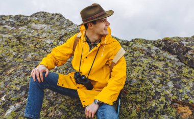 büyük taşlar üzerinde oturan neşeli mutlu yakışıklı yürüyüşçü