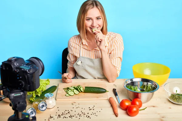 家族のためにおいしい昼食を調理しながら、かわいい主婦は新鮮なキュウリを噛みます — ストック写真