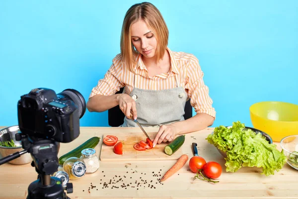 Roztomilá blondýnka, která krájí syrové rajčata pro kořeněnou omáčkou, vaří speciální večeři — Stock fotografie
