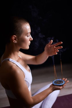 Genç, gülümseyen bir kadın sigara tüttüren bir sopayla rahatlıyor. aromaterapi, meditasyon