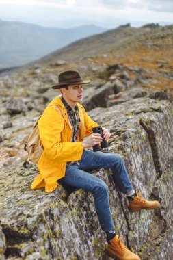 Genç adam zirvenin kenarında oturmuş gün batımını seyrediyor.