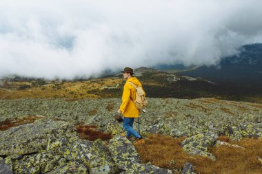 Sarı ceketli ve yeşil şapkalı genç adam yeni bir bölgeyi keşfediyor.
