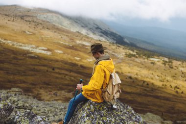 Mutsuz, kederli gezgin taşın üzerine oturmuş, aşağıya bakıyor.