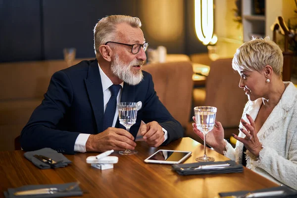 Atractiva pareja de ancianos sentados en la mesa del restaurante y hablando —  Fotos de Stock