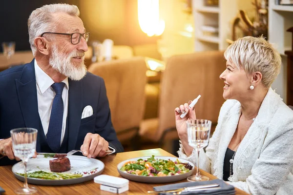 Senior σύγχρονο ζευγάρι λαμβάνοντας ένα γεύμα στο εστιατόριο χρησιμοποιώντας Iqos, ηλεκτρονικό τσιγάρο — Φωτογραφία Αρχείου