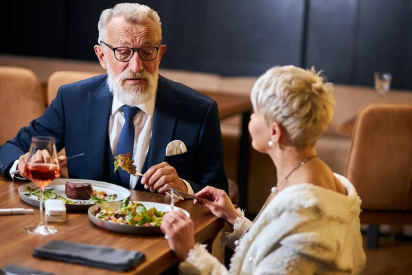 Pretty lady and elderly man having friendly conversation in restaurant