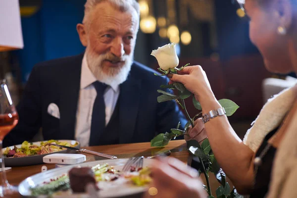 Sevgi dolu bir adam kadınına beyaz çiçek sunar. Restoranda yıldönümü kutlayan çift — Stok fotoğraf