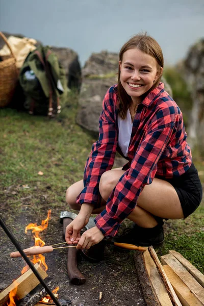 Charmant lachend meisje koken worsten op kamp — Stockfoto