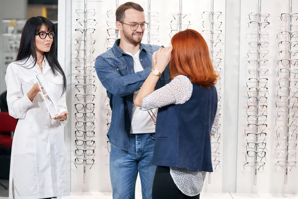 Mujer pelirroja se está probando un nuevo par de gafas, su novio la está ayudando —  Fotos de Stock