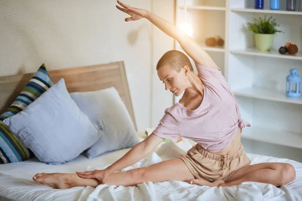 Flexível mulher de cabelos curtos na cama branca praticando ioga — Fotografia de Stock